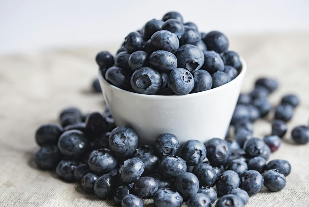 A white bowl heaped with fresh blueberries, more scattered on a linen cloth