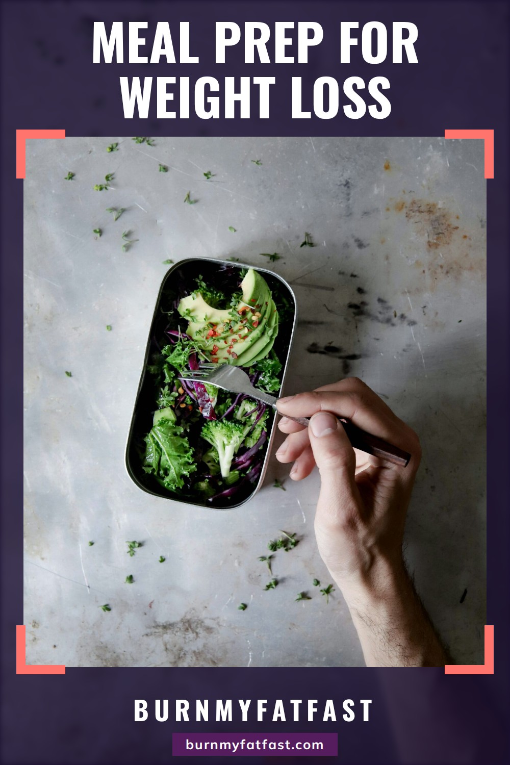 A hand with a fork reaching into a steel lunch tin packed with greens, broccoli, red cabbage and sliced avocado on a grey table