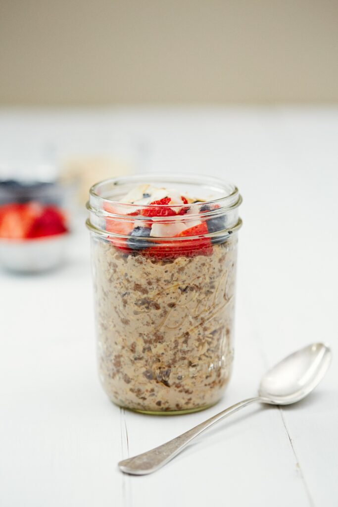 A mason jar of overnight oats topped with strawberries, blueberries and coconut flakes, a spoon beside it