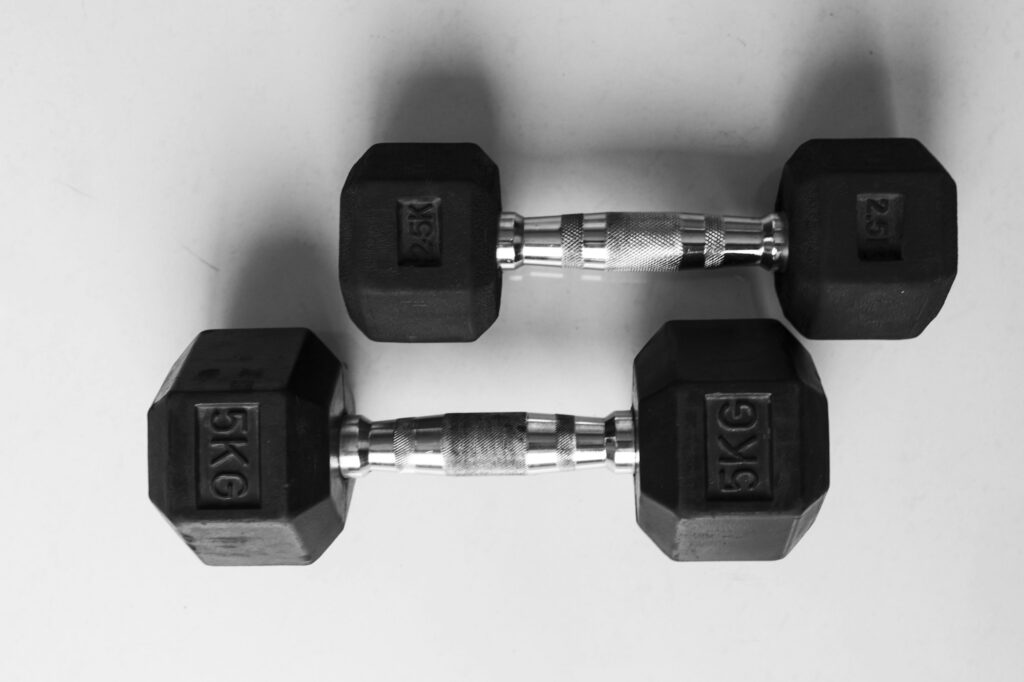 Two pairs of black hex dumbbells marked 5 kg and 2.5 kg lying on a white floor
