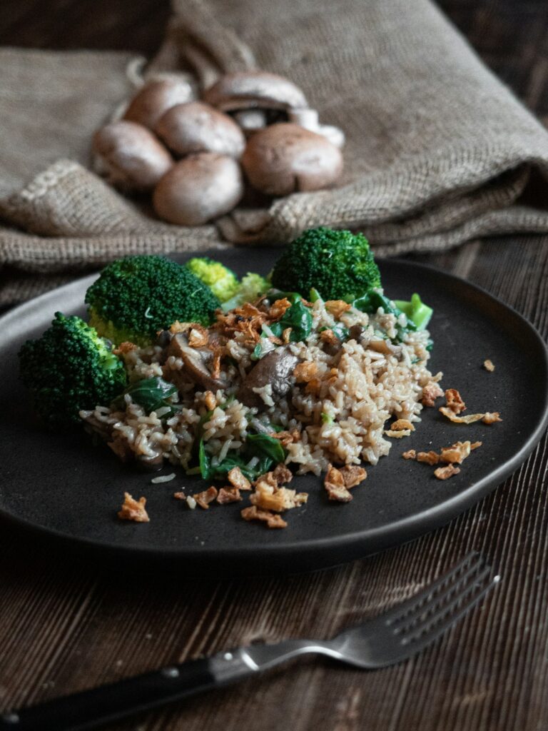 Brown rice with mushrooms and spinach and steamed broccoli florets on a dark plate, a fork beside it