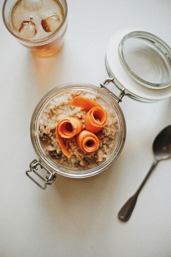 A glass clamp-lid jar of oats topped with carrot ribbons, the lid open, a spoon beside it