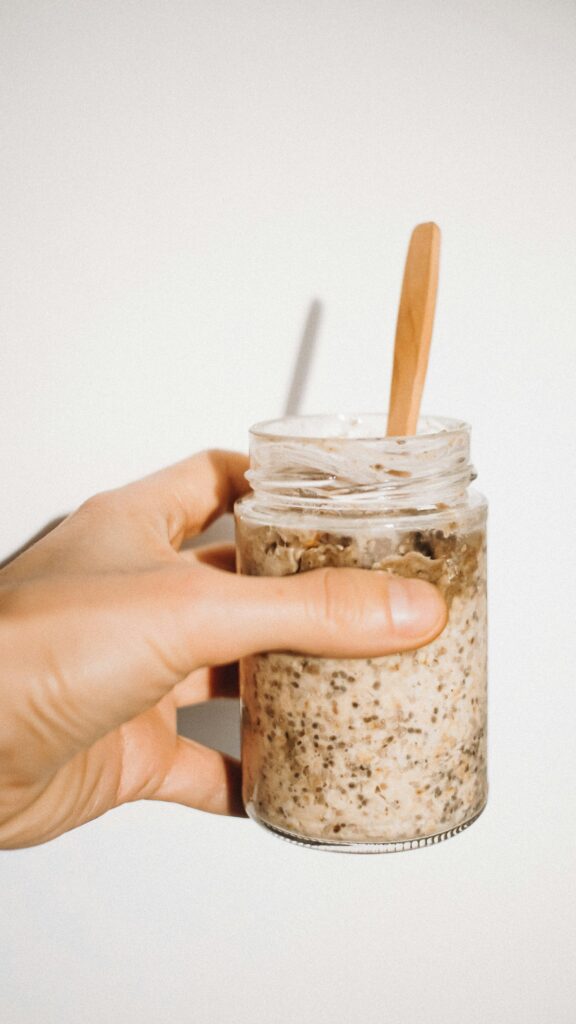 A hand holding a jar of chia overnight oats with a wooden spoon in it