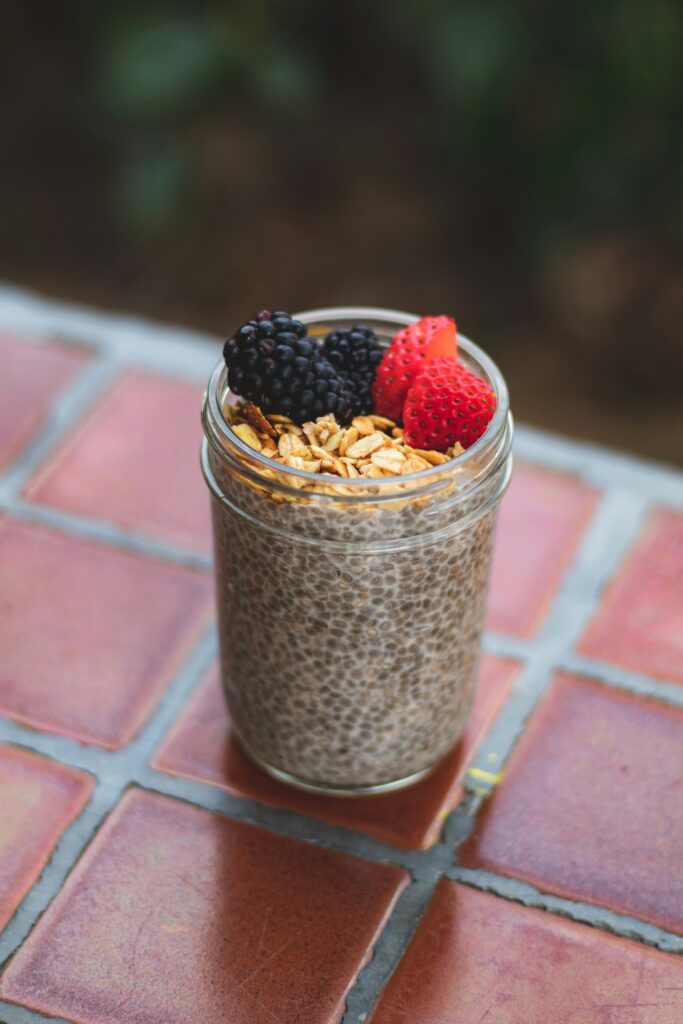A jar of chia pudding topped with granola, blackberries and strawberries on a red tile table