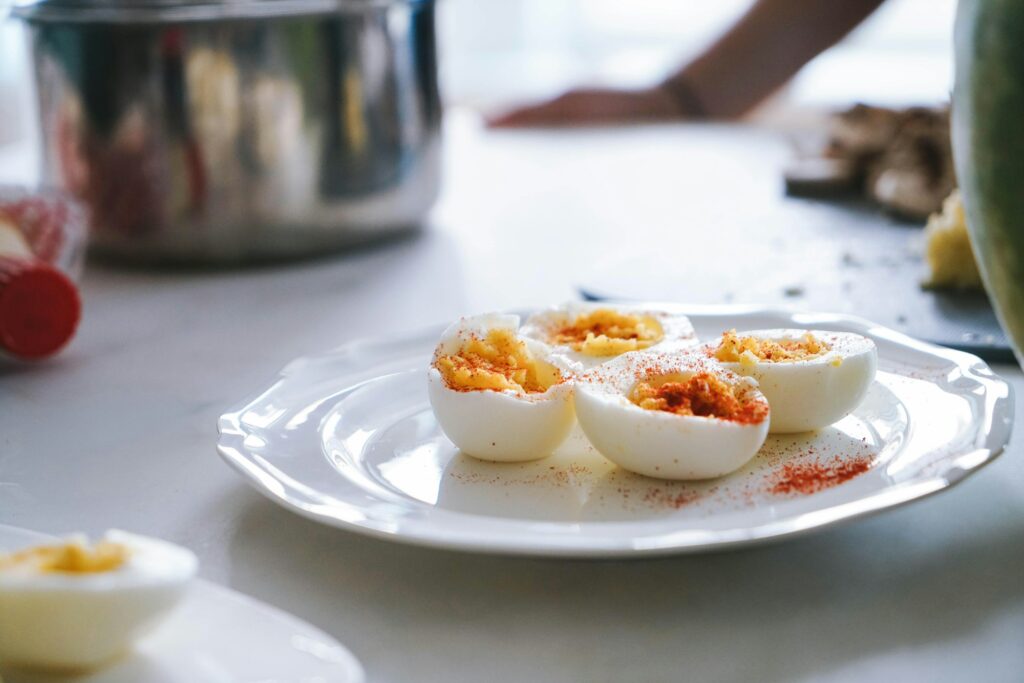 Halved hard-boiled eggs dusted with paprika on a white plate in a kitchen, a steel pot behind