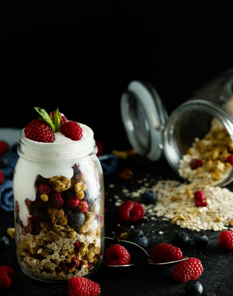 A glass jar layered with yogurt, granola and berries, topped with raspberries and mint