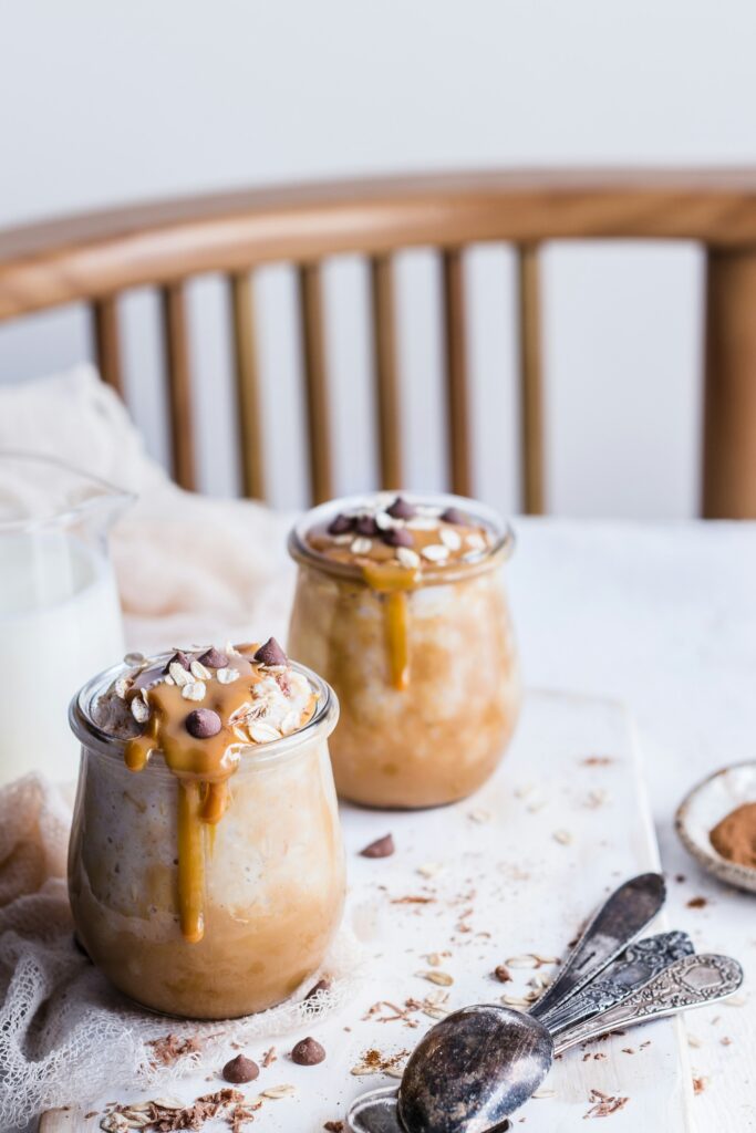 Two jars of oatmeal topped with a caramel-colored drizzle, rolled oats and chocolate chips